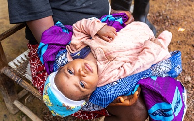 Rose sits quietly on her mother Annie Sackie’s lap after receiving the oral polio vaccine during a door-to-door immunization campaign in Bong County, Liberia, on July 30, 2025.